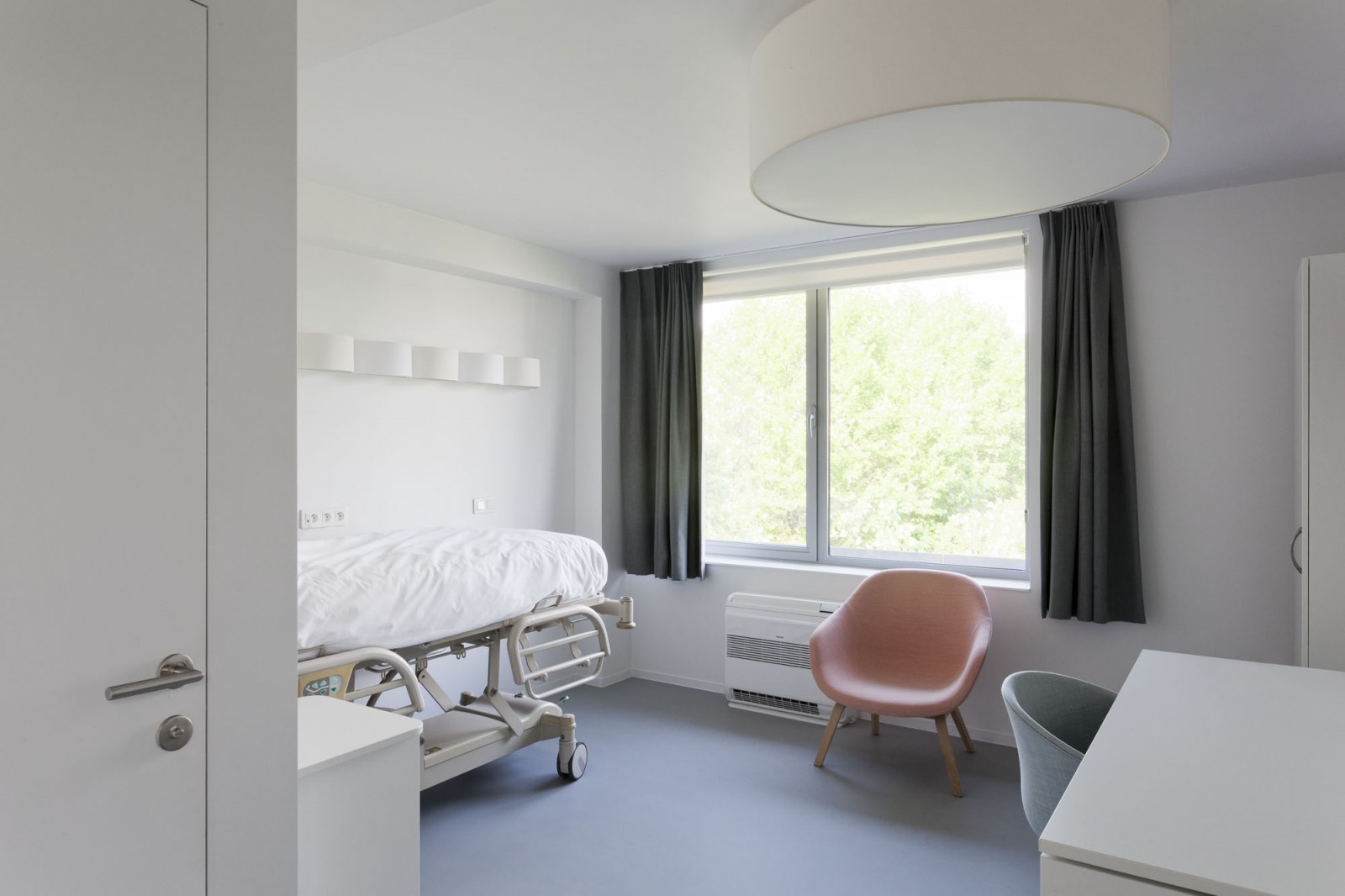 A single room in the guesthouse at o2 Clinic, including a hospital bed, desk and wardrobe.
